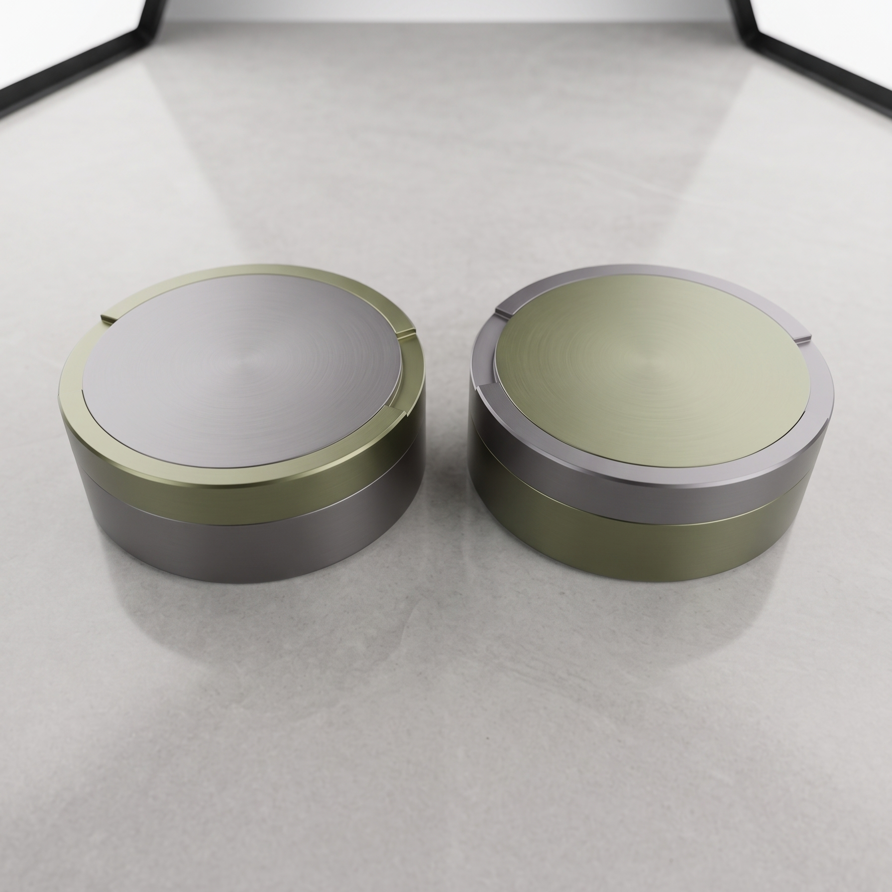 En parbild med två runda metalldosor i storlek large, sida vid sida på en ljusgrå yta. En dosa är olivgrön med grå ring, den andra är grå med en olivgrön ring. 