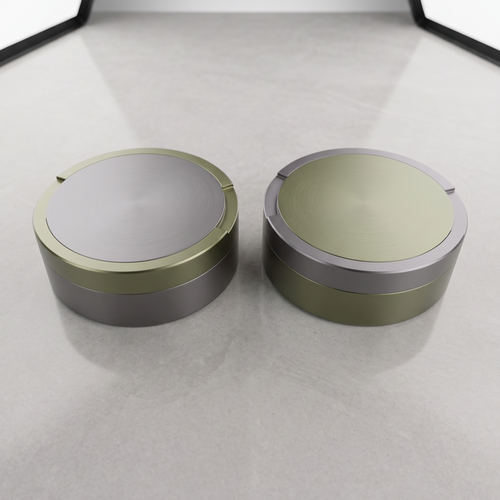 En parbild med två runda metalldosor i storlek large, sida vid sida på en ljusgrå yta. En dosa är olivgrön med grå ring, den andra är grå med en olivgrön ring. 
